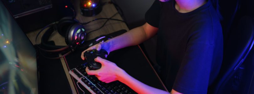 Female cyber hacker gamer playing or streaming video games on computer with joystick in neon light