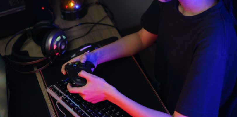 Female cyber hacker gamer playing or streaming video games on computer with joystick in neon light